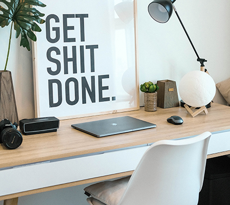 Social media coaching: Art behind desk workspace with laptop, art displays text "get sh** done"
