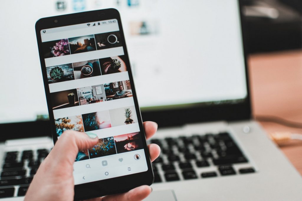 The Top 3 Social Media Tools Every Entrepreneur Needs - woman holding cell phone with image grid and blurred image of a laptop behind it
